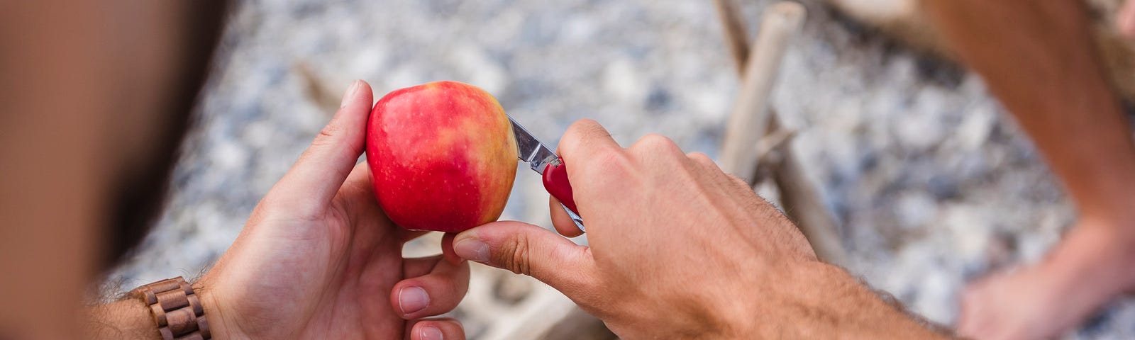 Person using pocket knife to peel apple skin.