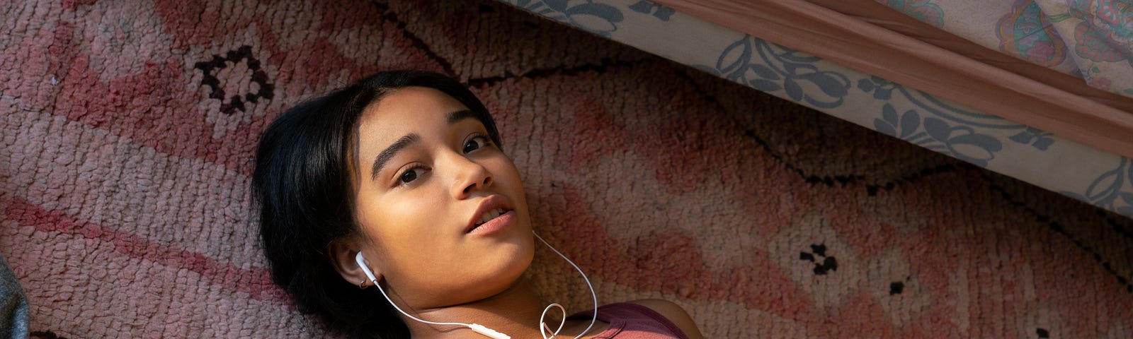 A still of Amandla Stenberg laying on a rug listening to music through white earphones in the Netflix show “The Eddy.”