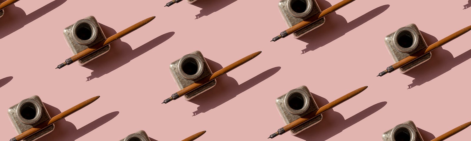 A photo of many antique ink pens lined up on a pink background.