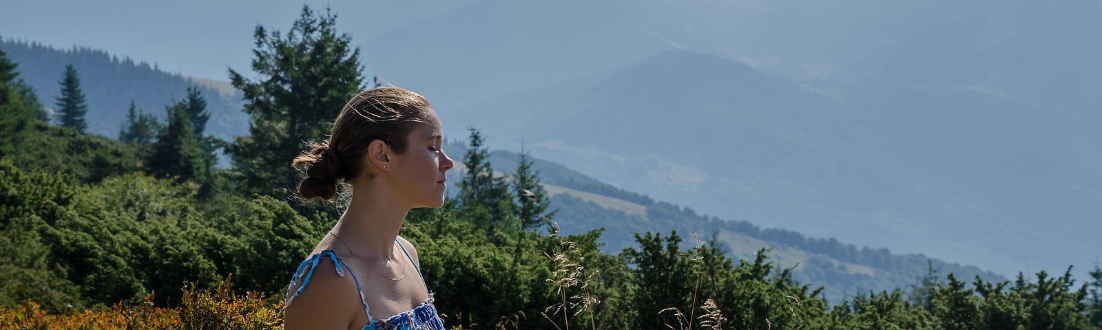 A young woman sits on a sunny hill side while meditating