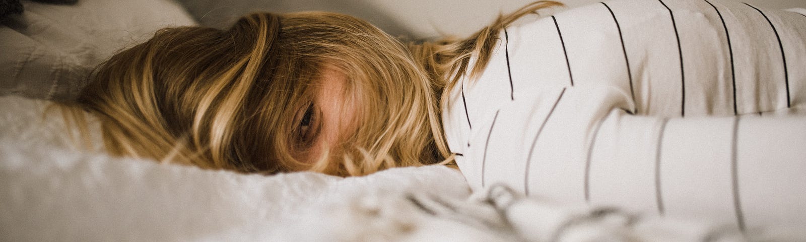 Tired woman, face down on bed, looking through half-open eyes toward the viewer.