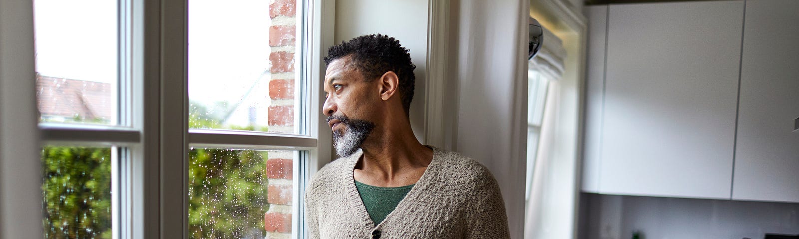 Pensive older man holding mug while looking outside.