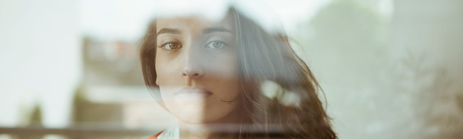 Woman looking out the window with reflection of outdoors.