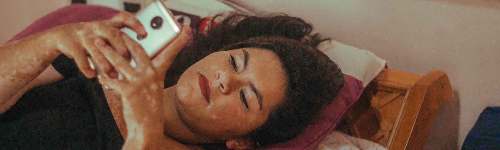 A photo of a young woman lying in bed, texting on her phone.