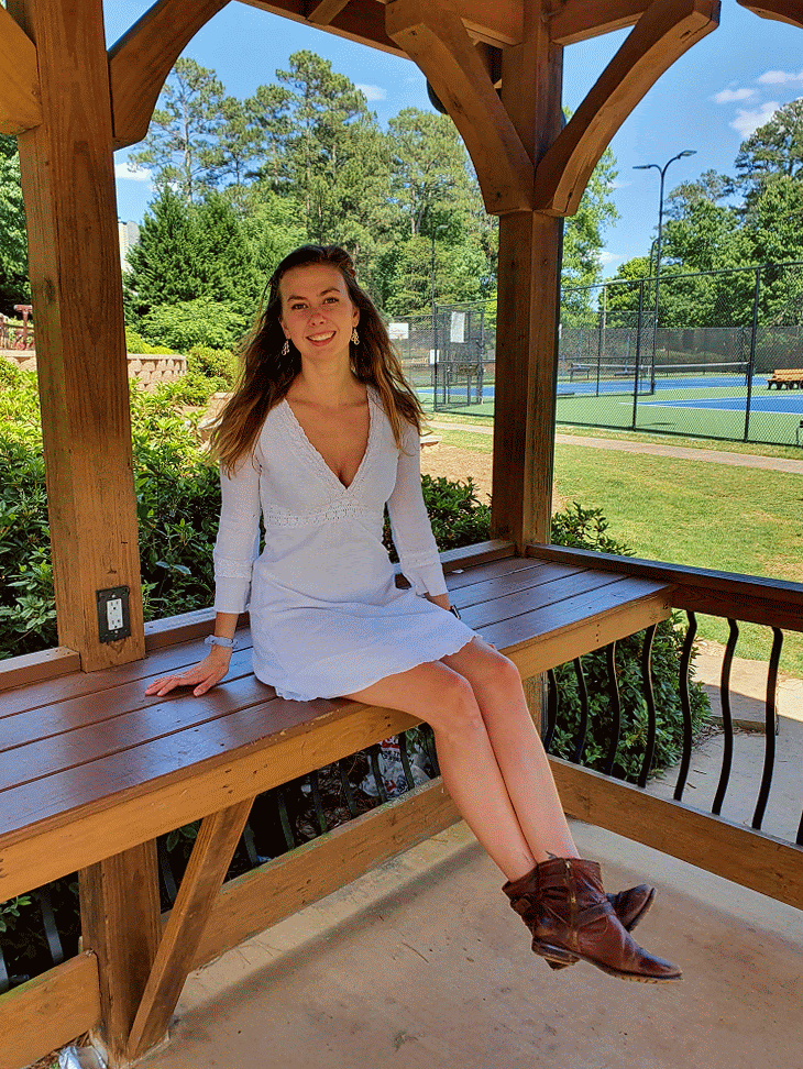 Author swings her legs in a white dress outdoors in a pavilion.