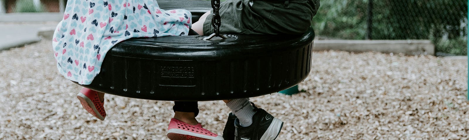 A little boy and a little girl sitting on a tire swing together