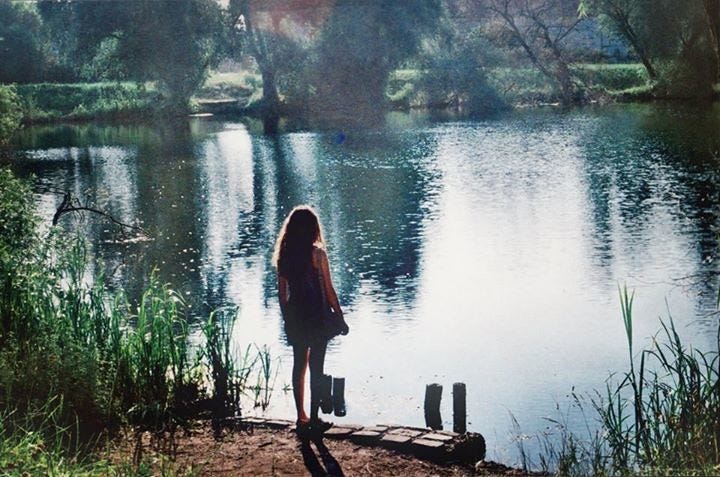 A photo of the back of a woman standing in front of a lake.