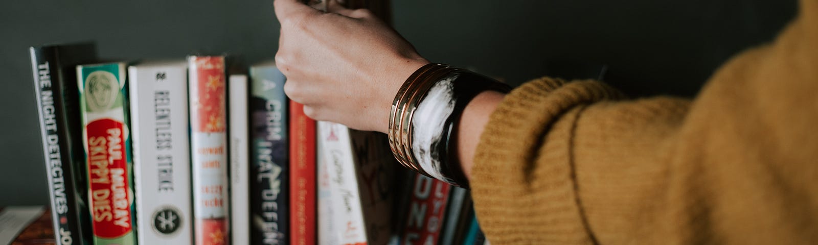 A hand is reaching out and taking a book from a bookshelf.