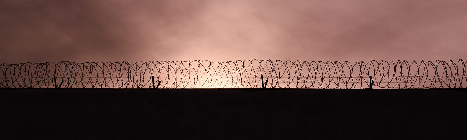 A photo of a barbed wire fence against a sunset sky.