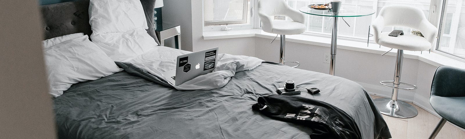 Hotel room with laptop in unmade bed and breakfast on table