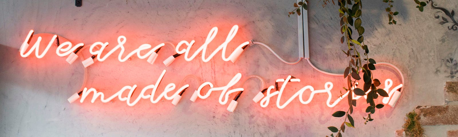 neon sign under bookshelf saying “We are all made of stories”