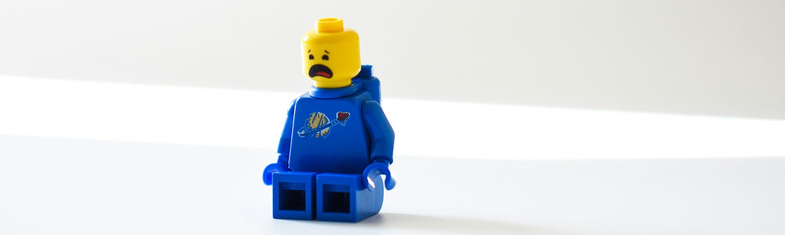 A Lego astronaut in a blue uniform with a scared expression. The pictures background is white.