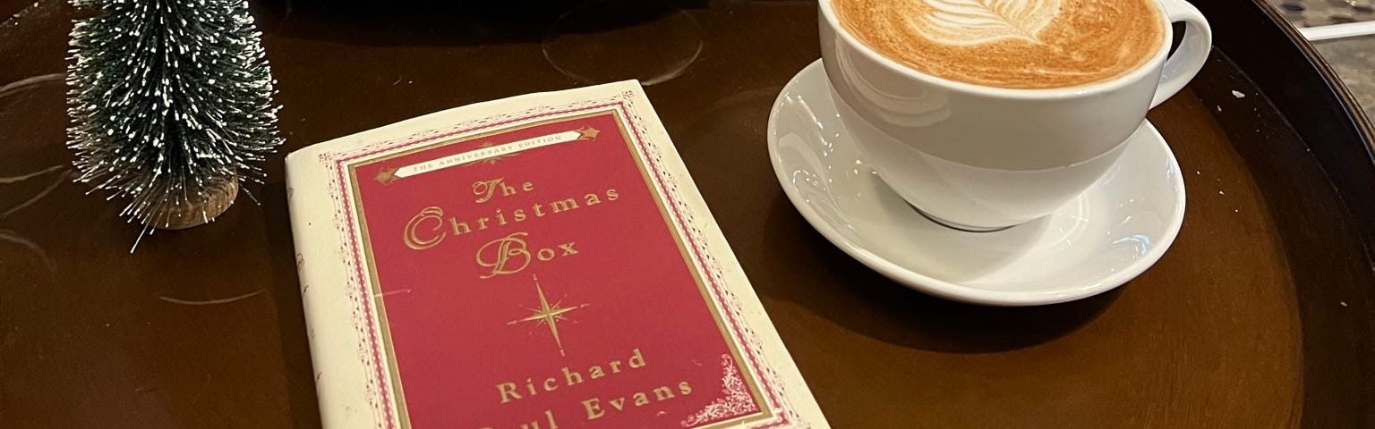Christmas book on table beside coffee with Christmas tree in background.