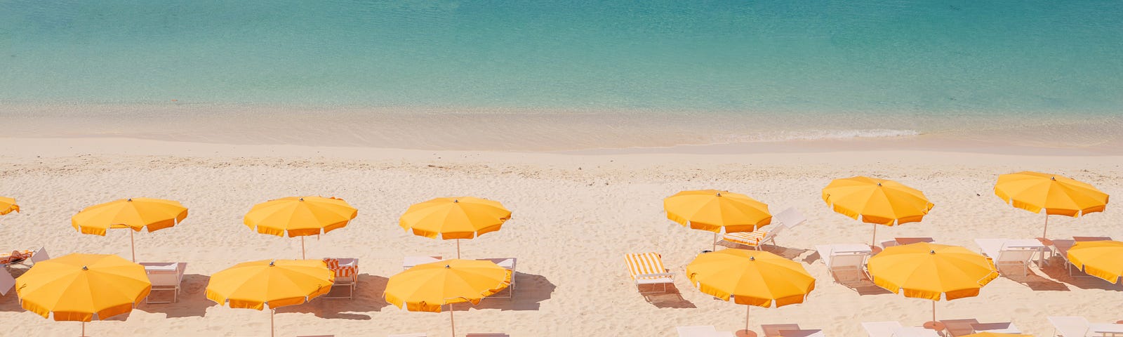 A beach with two rows of large yellow umbrellas, with a clear blue ocean in the background.