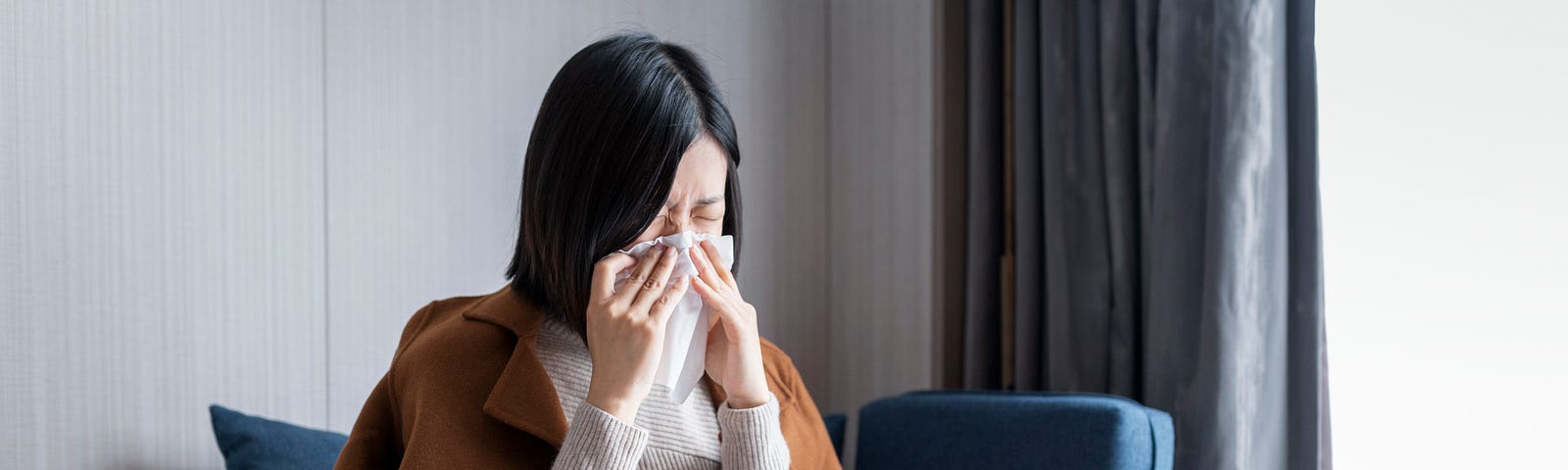 A woman sneezes into a tissue and wipes her nose.