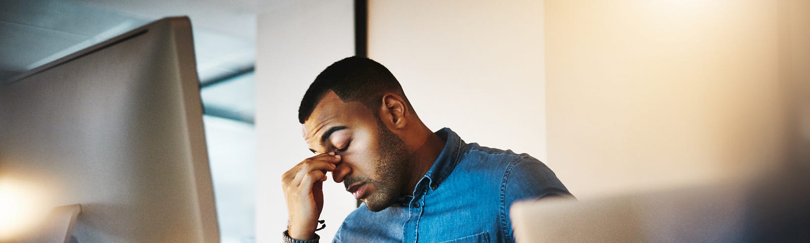 A young businessman experiences stress late at night at his work station computer.