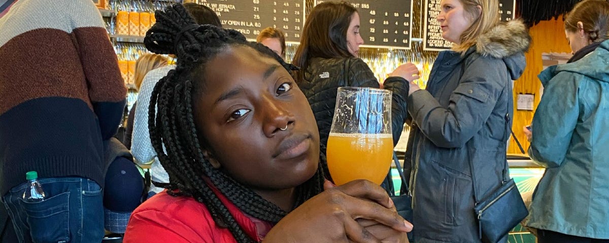 Nikita Richardson holding a glass of orange juice in a cafe, with people in line behind her.