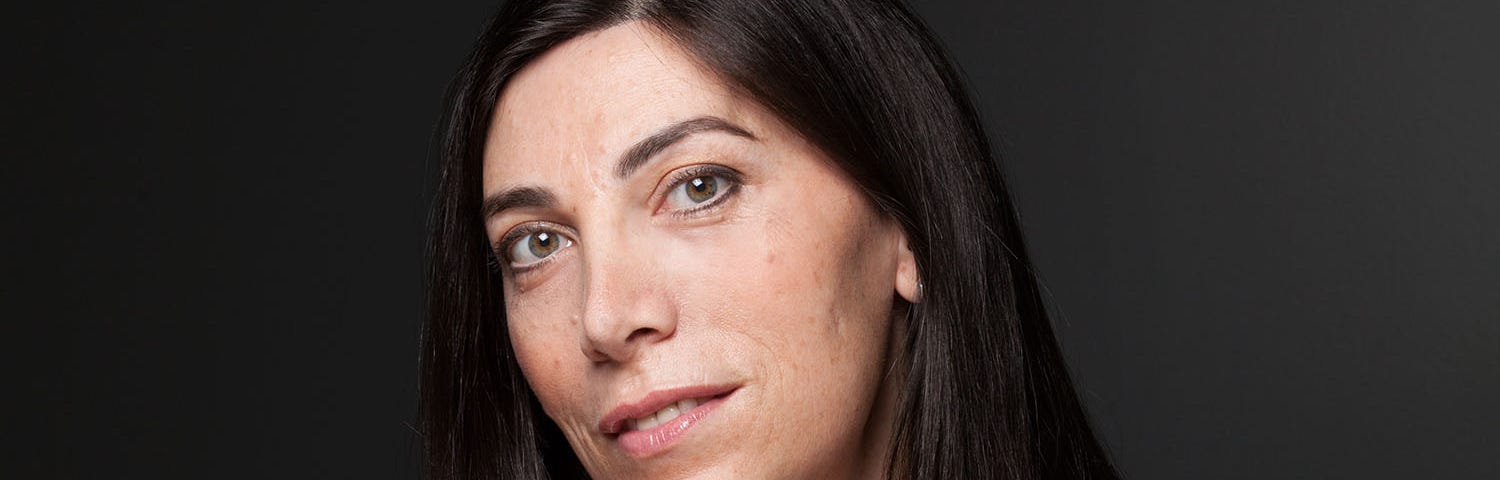 A portrait photo of Emily Leproust seated with her arms crossed at a wooden table. Leproust is CEO of Twist Bioscience.