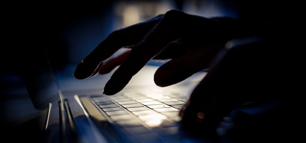 Shadowy hands write on a computer keyboard, symbolizing hackers and data security.