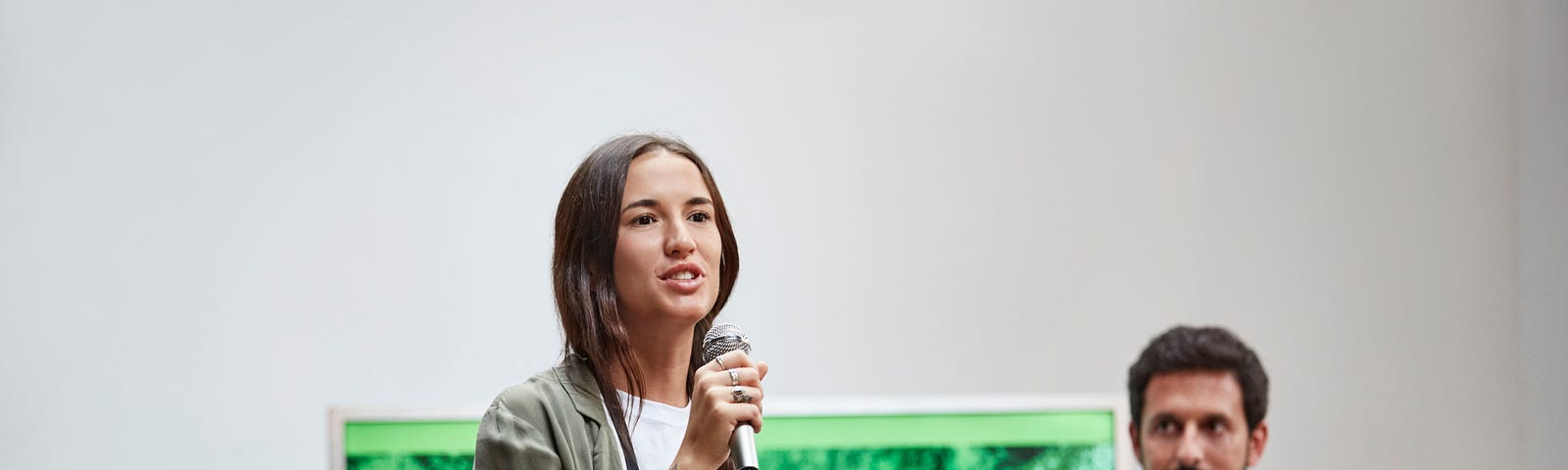 A woman speaks into a microphone, asking questions while standing amidst colleagues.