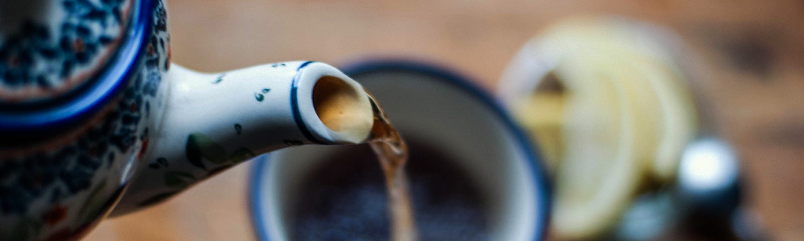 Pouring tea into a tea cup from a tea kettle.