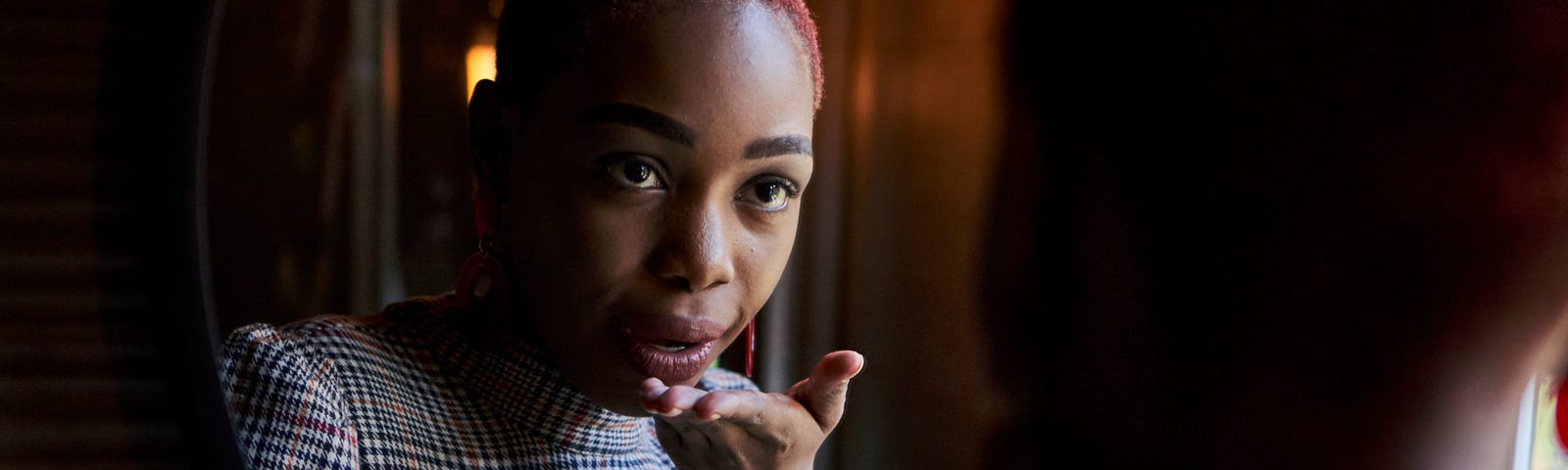 A photo of a stylish young black woman blowing herself a kiss in the mirror.