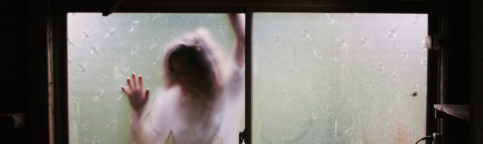 Blurred image of a woman with her hands placed against a window. Spooky, creepy, trapped feeling.