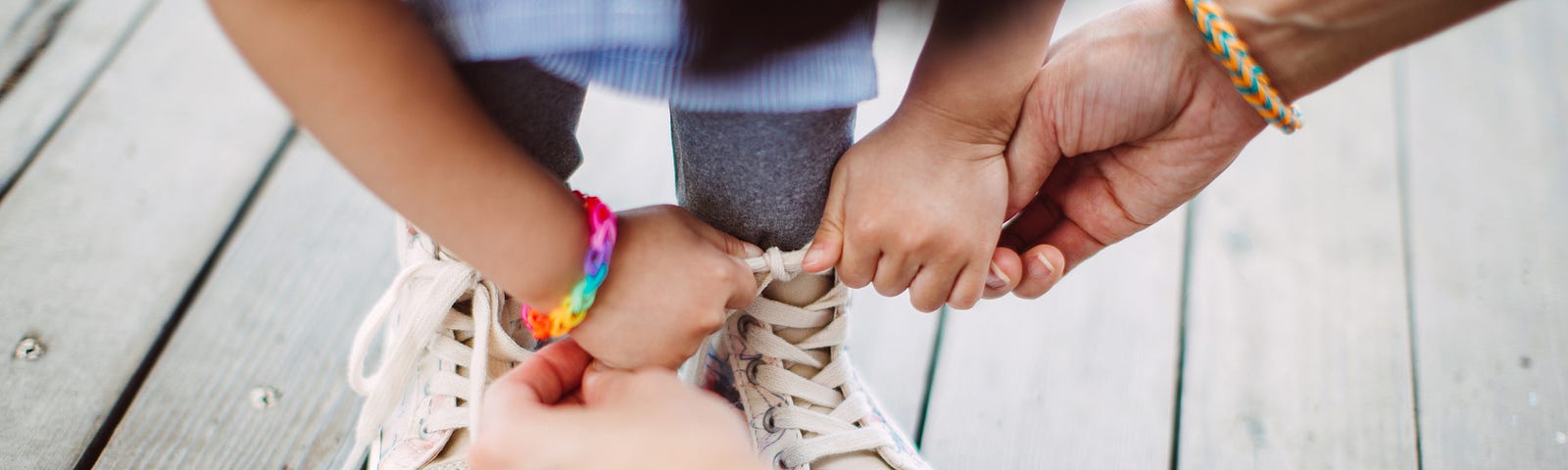 A parent helps a child tie their shoelaces.