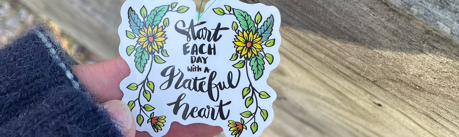 Tag hanging on a fence that reads, “start each day with a grateful heart.”