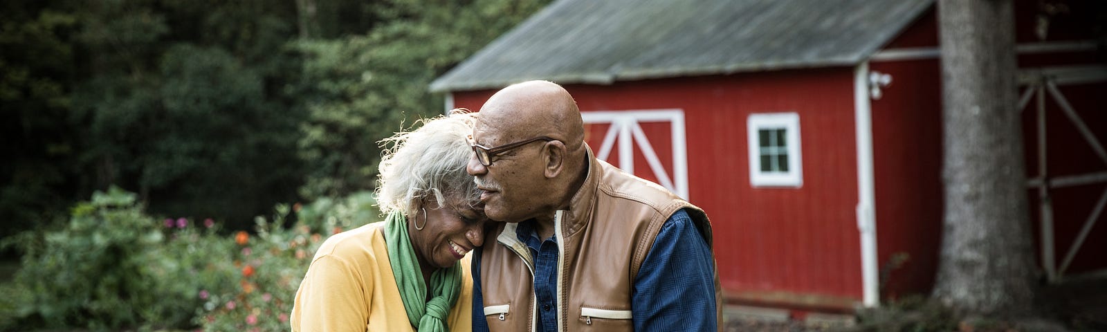 A photo of an elderly black couple in front of a barn-looking structure in a rural area.