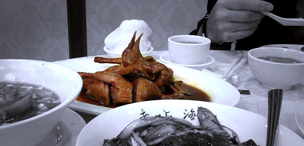 A black-and-white photo where the only colored element is a sliced up pigeon served on a lunch plate.