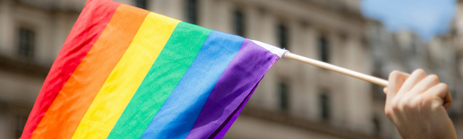 A hand waving a rainbow pride flag.