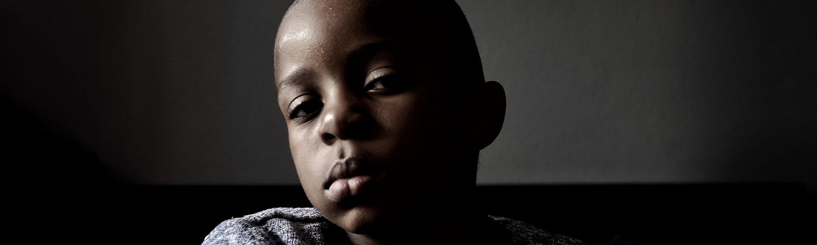 Shadowy portrait of a Black child with shaved hair.