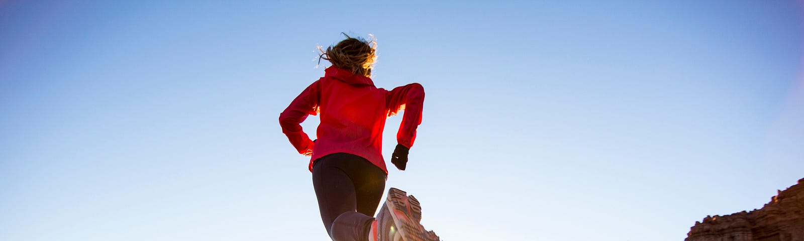 A photo of a woman running on a desert trail, her left foot kicking up dirt.