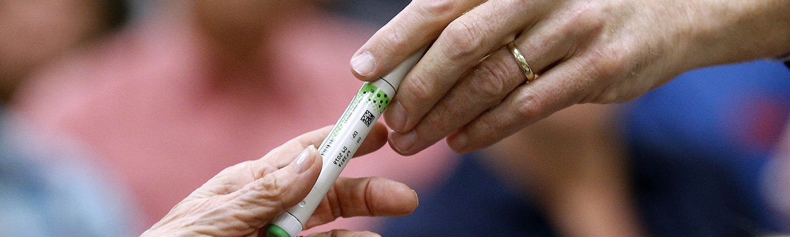 A close up shot of a woman’s hand passing on an insulin pen to Sen. Bill Cassidy (R-LA) during a town hall in 2017.