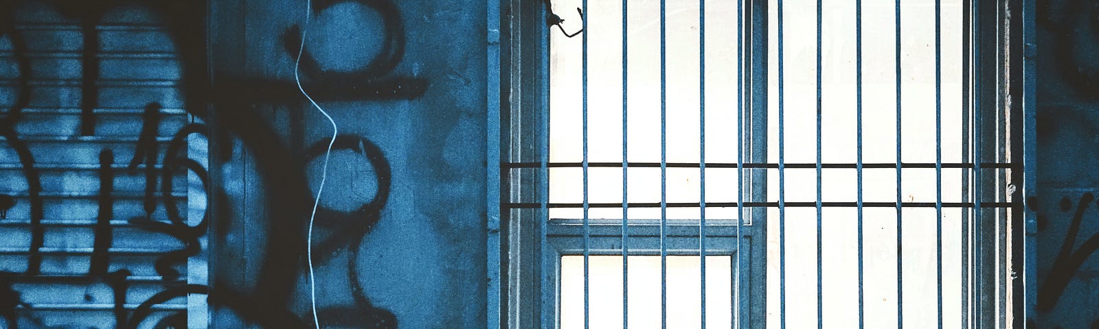 Photo of window with bars. Wall next to window is covered with grafitti.