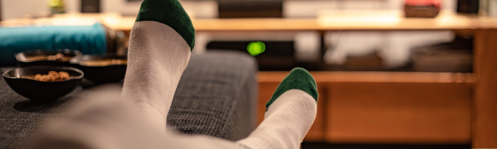 View of person’s crossed legs/feet on the sofa with TV in background.