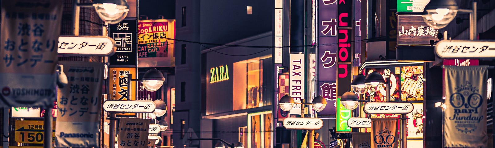 A busy street with neon signs, filled with shops and shoppers.