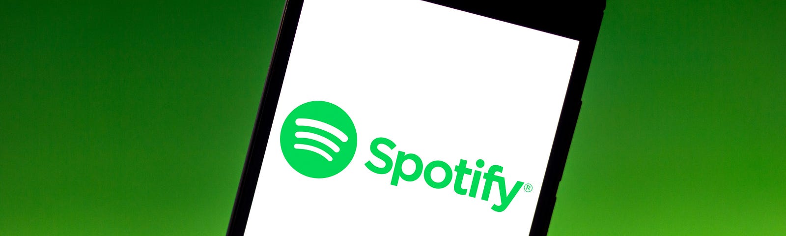 The Spotify logo is seen displayed on a smartphone, held up against a black-to-green gradient background.