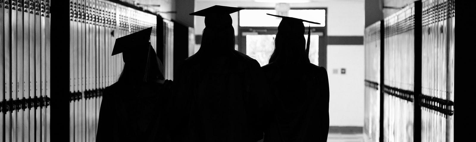 A black and white picture of three high school grads walking down the school hallway wearing their grad gowns.