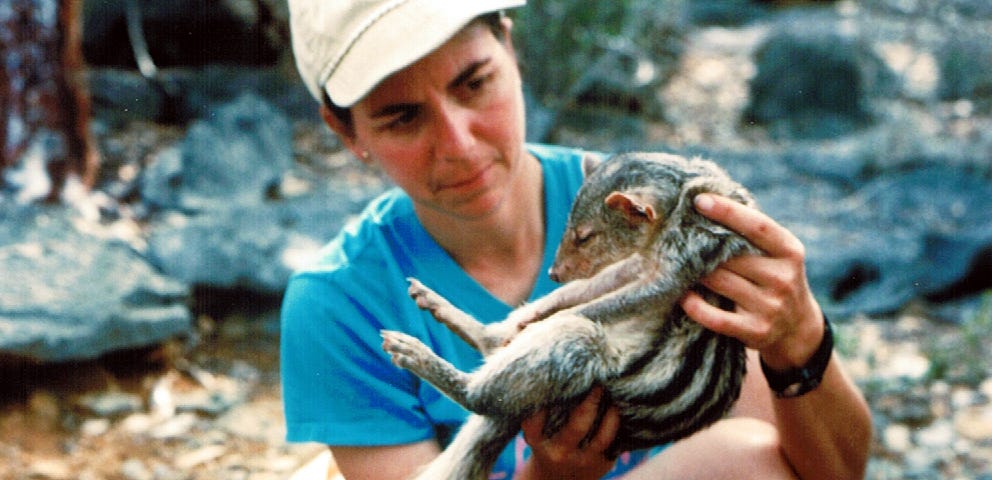 A woman holds an small furry animal with a fluffy tail