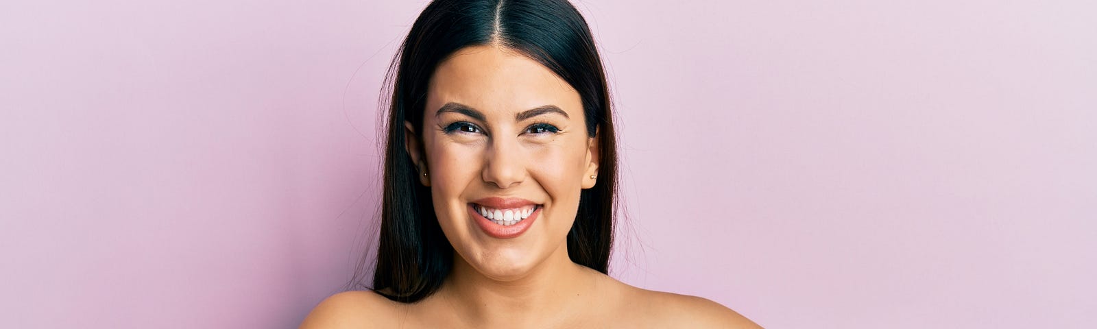 A latino woman covers her breasts and smiles at the camera.