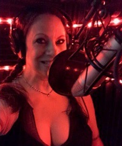 a photo of Karen Falcon in her sound room with red lights and sitting in front of her microphone