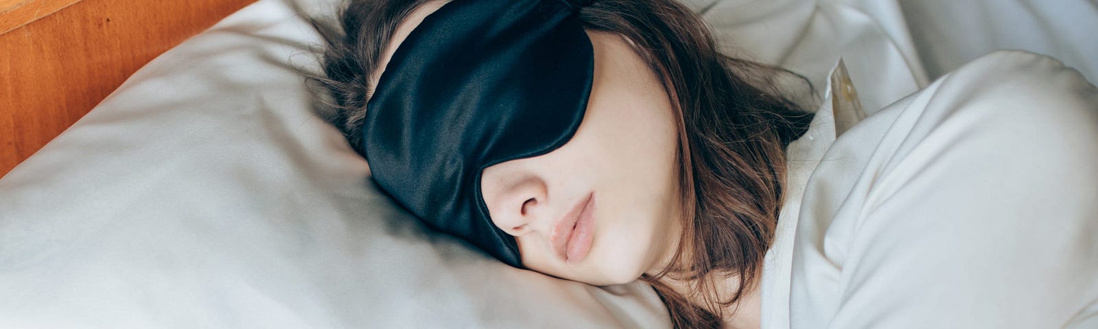 A woman wears a sleeping mask while in bed.