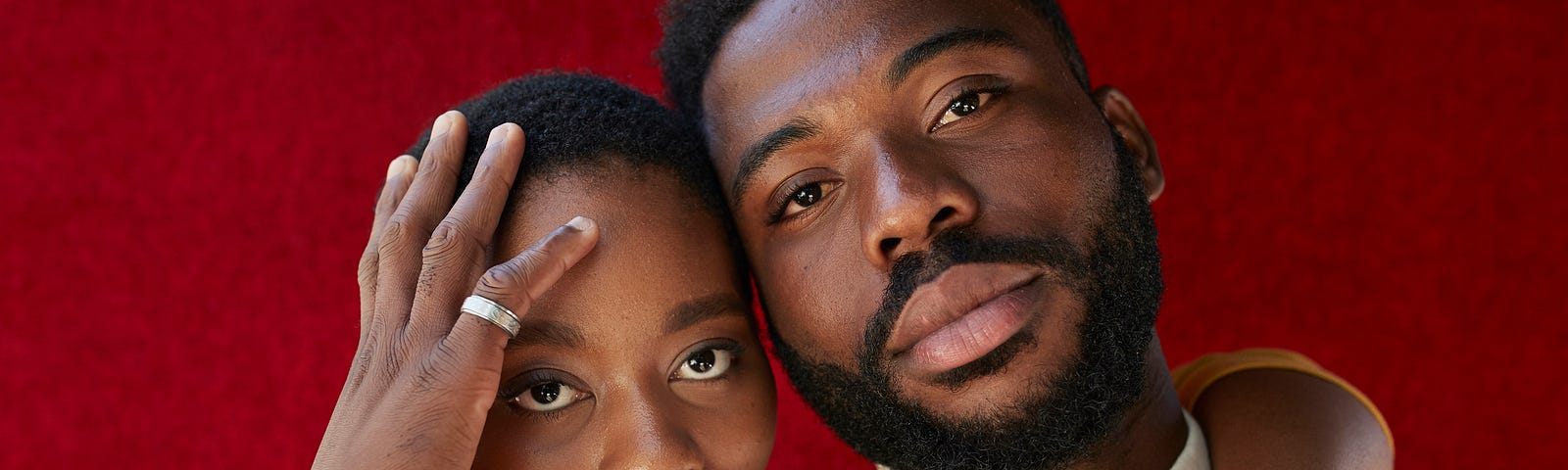 Black man and woman posing together in front of a maroon background.