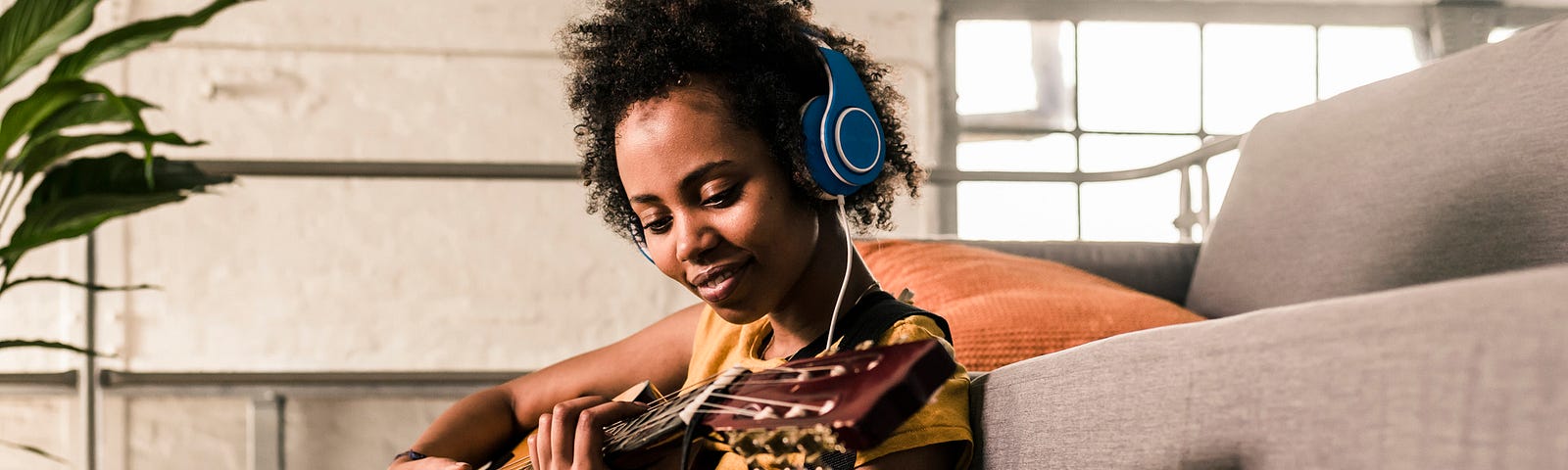 A Black woman learning to play the guitar from an online video.