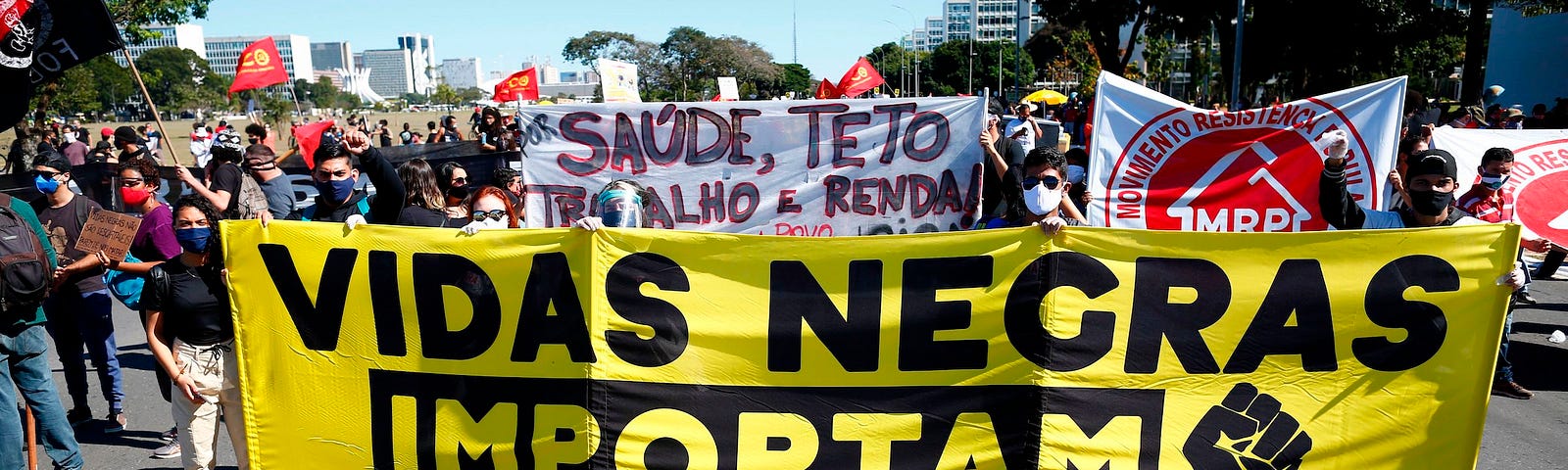 Protesters behind a large black-and-yellow banner that reads “Vidas Negras Importam” (“Black Lives Matter” in Portuguese).