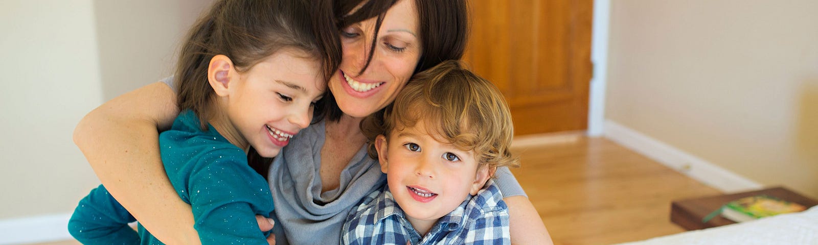 A parent hugging two children in their house.