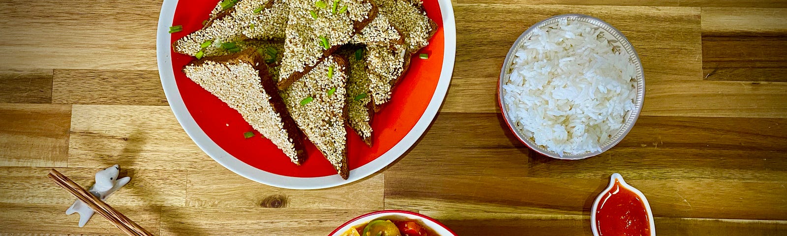 A spread of toast triangles coated in sesame seeds, warm red sweet and sour tofu, and white rice