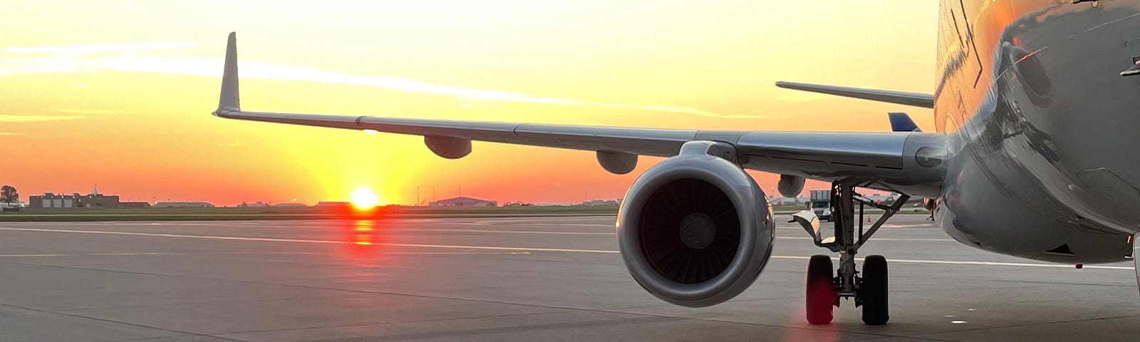 Sunrising underneath the wing of a jet aircraft parked on the ramp.